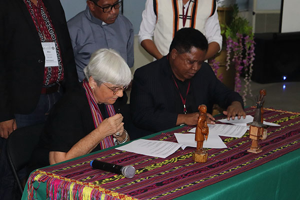 Christine Vertucci and Fr. Julio Crispim Ximenes Belo sitting at table signing the MoA